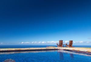 2 Stühle und ein Pool mit Meerblick in der Unterkunft Holualoa Inn in Kailua-Kona