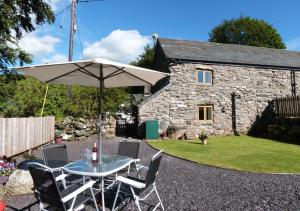 a table with an umbrella in front of a stone cottage at Crud y Wennol in Llandderfel