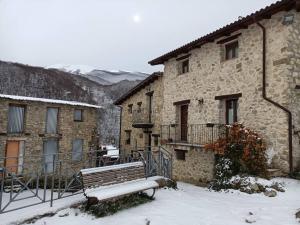 un bâtiment en pierre avec un banc dans la neige dans l'établissement La casa della Rocca, 