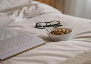a bowl of cereal and a book and glasses on a bed at Hotel Ponta Verde Praia do Francês in Praia do Frances