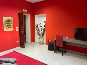 Habitación con pared roja, escritorio y TV. en B&B La Stazione en Sibari