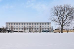 Fairfield by Marriott Hokkaido Eniwa في Eniwa: عماره فيها شجره امام حقل ثلجي مغطى