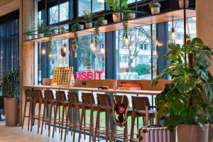 a restaurant with a bar with chairs and plants at Moxy Duesseldorf South in Düsseldorf
