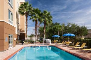 una piscina con sillas, sombrillas y palmeras en Fairfield Inn & Suites Jacksonville Butler Boulevard en Jacksonville