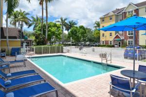 una piscina con sillas, una mesa y una sombrilla en TownePlace Suites Miami West Doral Area, en Miami