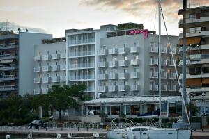 un grand hôtel blanc avec un bateau devant lui dans l'établissement Moxy Patra Marina, à Patras