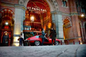 Un uomo e una donna che passano davanti a un'auto rossa davanti a un edificio. di St. Pancras Renaissance Hotel London a Londra