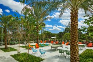 un patio con mesas, sillas y palmeras en Aloft Miami Airport en Miami