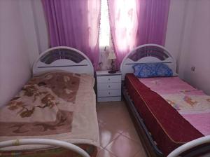 two beds in a small room with purple curtains at Maison Latifa in Oujda