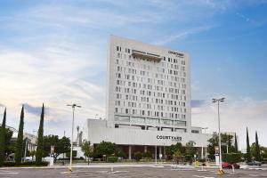 een hoog wit gebouw met een parkeerplaats ervoor bij Courtyard by Marriott Leon at The Poliforum in León