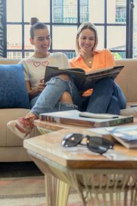 Dos mujeres sentadas en un sofá leyendo un libro en Ventiuna Hotel y Coliving, en Pereira