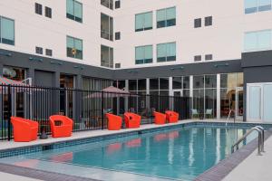 a swimming pool with red chairs and a building at Aloft Houston Shenandoah - The Woodlands in Shenandoah