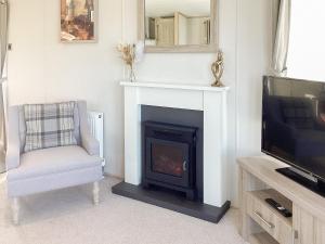 a living room with a fireplace and a chair and a tv at Ballagan Lodge in Leanach