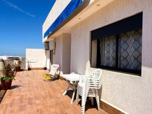 a patio with white chairs and a table on a balcony at Appartement Amwaj in Plage de Mehdia