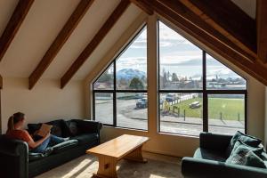 una mujer sentada en un sofá leyendo un libro en una habitación con ventanas en Snow Denn Lodge, en Methven