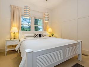 a white bedroom with a large bed and two windows at Leura Country Cottage in Leura
