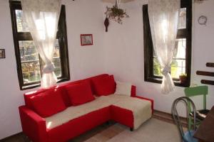 a red couch in a living room with windows at Глинената къща в Дълги Дел in Dŭlgi Del