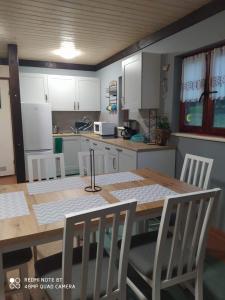 una cocina con mesa y sillas y una cocina con armarios blancos. en Agroturystyka Giże - domek letni en Ełk