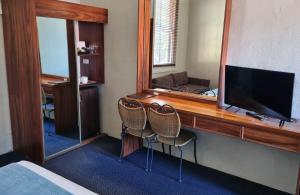 a bedroom with a desk with a television and two chairs at Seaton Arms Motor Inn in Albury