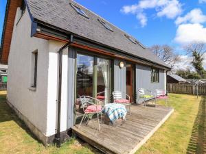 a house with a deck with chairs and a table at Brodie East Cottage in Forres