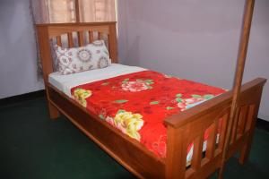 Cama de madera con manta roja y almohada en Kili View Lodge, en Moshi