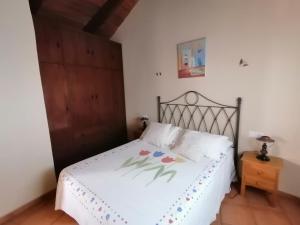 1 dormitorio con cama blanca y puerta de madera en La casita de la abuela isabel, en Ubrique