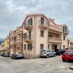 duży różowy budynek z samochodami zaparkowanymi na parkingu w obiekcie Valeria's Apartment w mieście Argostoli