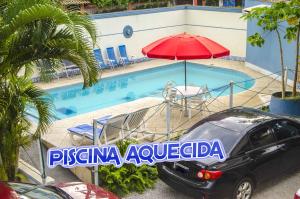 a car parked next to a swimming pool with a red umbrella at Hotel Pousada Iracemar - Guarujá in Guarujá