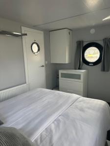 1 dormitorio con cama blanca y ventana en Stoere HOUSEBOAT op toplocatie!, en Belt-Schutsloot
