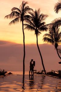 una pareja de pie en el agua bajo palmeras en la playa en Kupu Kupu Phangan Beach Villas & Spa by L'Occitane - SHA Plus en Haad Pleayleam