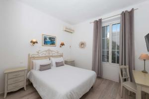a white bedroom with a bed and a desk and a window at Hôtel Beau Site - Cap d'Antibes in Antibes