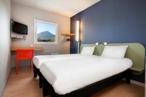 um quarto de hotel com duas camas e uma secretária em ibis budget Clermont Ferrand Nord Riom em Riom