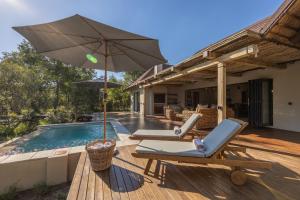 una terraza con 2 sillas y una sombrilla junto a la piscina en Ukanyi Luxury Villa, en Hoedspruit