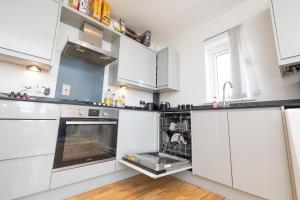 a kitchen with white cabinets and an open dishwasher at Newly refurbished apartment in Elmers End