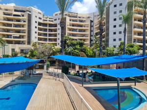 a pool with blue umbrellas in front of buildings at Amazing Apartment in Raanana & Swimming up to 4 guests pool and Jacuzzi in Ra‘ananna