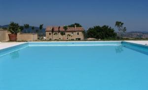 a large blue swimming pool with a house in the background at Agriturismo Colle delle Stelle in Mergo