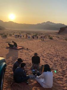 Un groupe de personnes assises sur le sable dans le désert dans l'établissement Martian desert Camp, à Wadi Rum