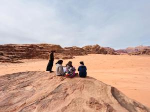 3 personnes assises sur un rocher dans le désert dans l'établissement Martian desert Camp, à Wadi Rum