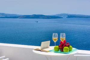 a table topped with a glass of wine and a plate of food at Kima Oia Suites in Oia