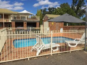 a fence with two chairs and an umbrella next to a pool at Golf Links Motel in Tamworth