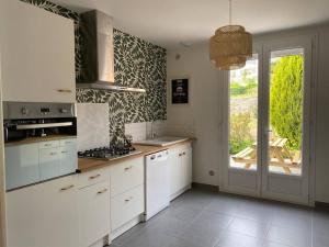 une cuisine avec des placards blancs et une grande fenêtre dans l'établissement Maison Village de La Verrerie, à Cherbourg en Cotentin