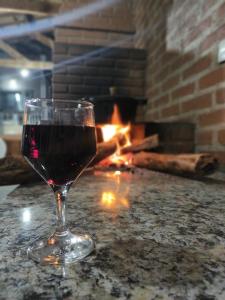 um copo de vinho sentado numa mesa em frente a uma lareira em Canto do Pássaro Aconcheg em São Bento do Sapucaí