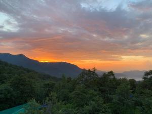 einen Sonnenuntergang in den Bergen mit Bäumen im Vordergrund in der Unterkunft The Loft Kohima 