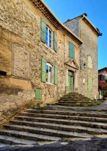 un antiguo edificio de piedra con persianas verdes y escaleras en La tour de Pezene en Anduze