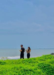 two men standing on a grassy hill next to the ocean at Flexi Lodge in Negombo