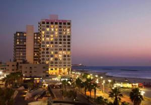 a tall building with lights in front of the ocean at Orchid Hotel Beachfront 2BR Apartment in Tel Aviv
