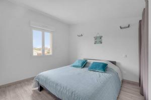 a white bedroom with a bed with two blue pillows at LA MEDITERRANEENNE in Quint-Fonsegrives