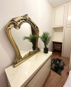 a gold mirror on top of a dresser with two plants at London Charm - Comfortable Room in Spacious House in London