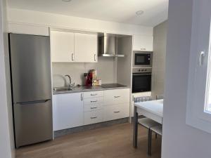 cocina con armarios blancos y nevera de acero inoxidable en Apartamento puerto en A Guarda