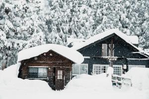 eine schneebedeckte Hütte mit Bäumen im Hintergrund in der Unterkunft Mountain Hut Myoko in Myōkō